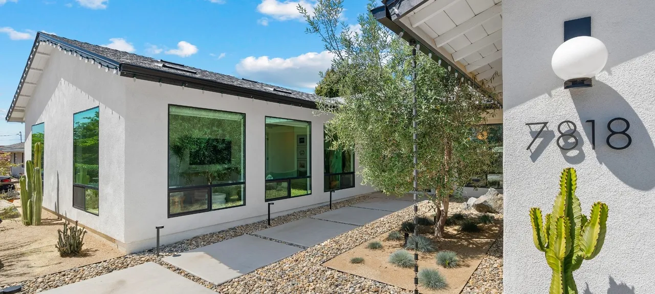 Modern single-story home addition exterior with white stucco, black-framed windows, and desert landscaping