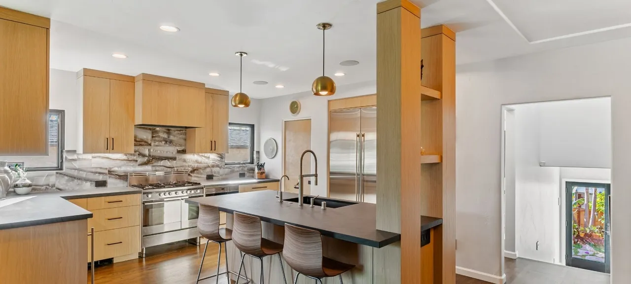 Kitchen addition remodel with wood cabinetry, stone slab backsplash, and center island seating