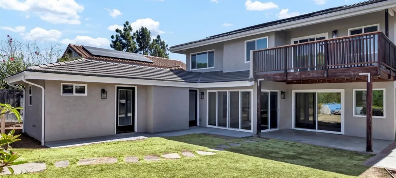 Two-story home addition with primary suite balcony and multiple sliding glass doors to the backyard
