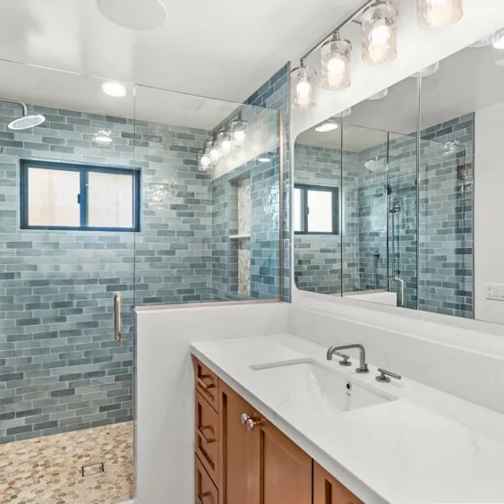 Aging-in-place bathroom remodel in San Diego with a curbless shower, blue tile, frameless glass, and recessed niche