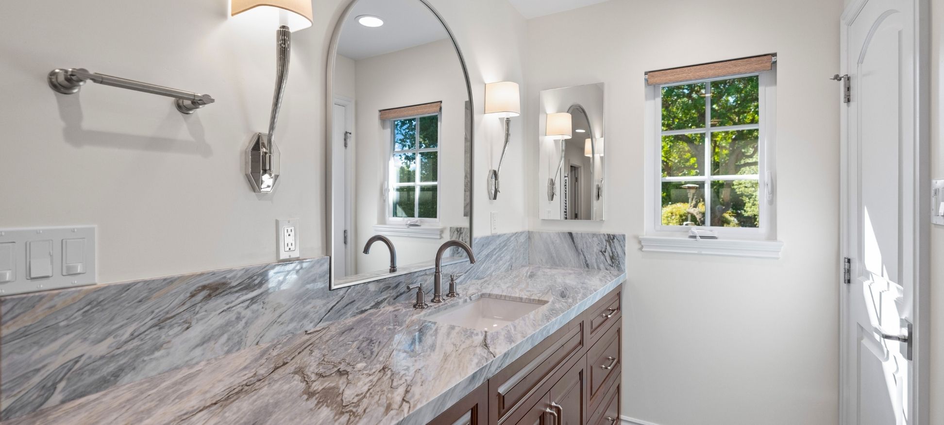Bathroom remodel with arched mirror, marble slab backsplash, and wood vanity