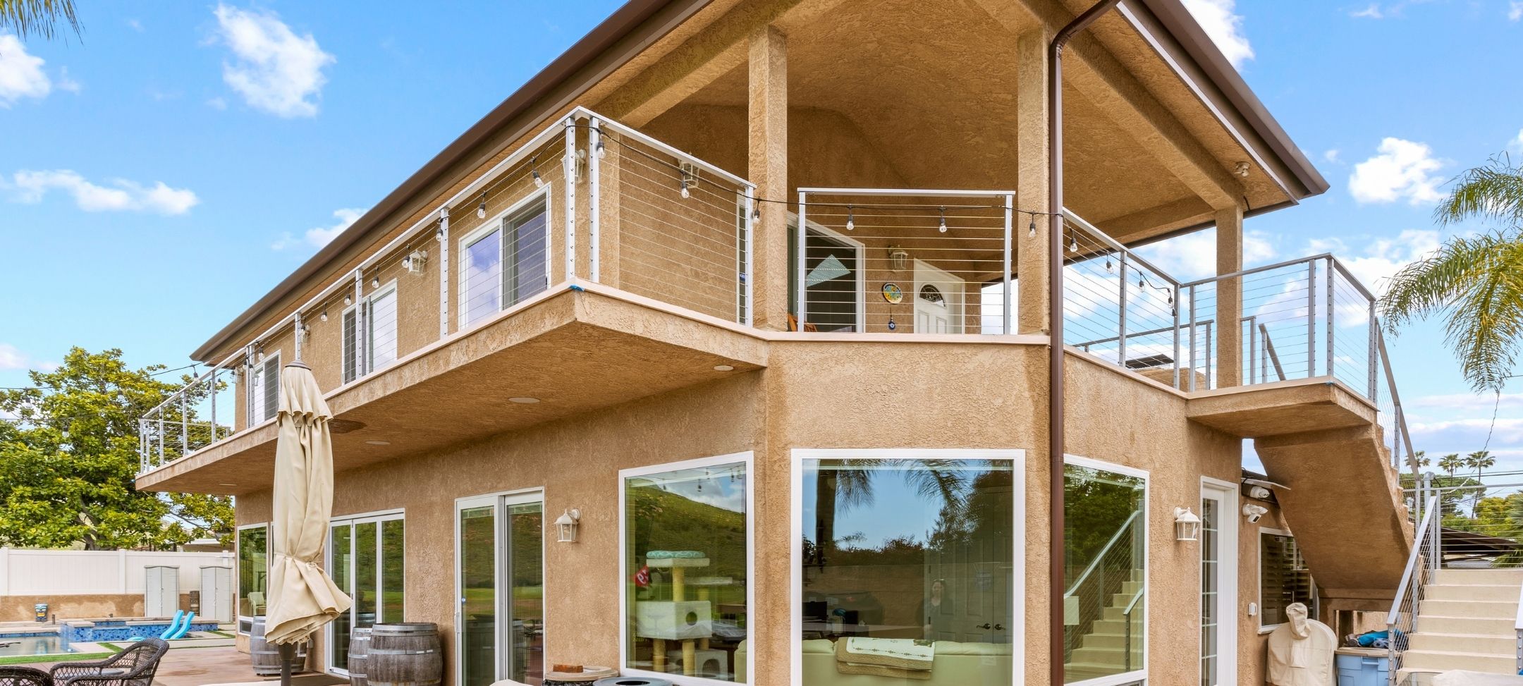 Custom home rear exterior with two-story cable-railed decks, string lights, and covered patio overlooking a pool
