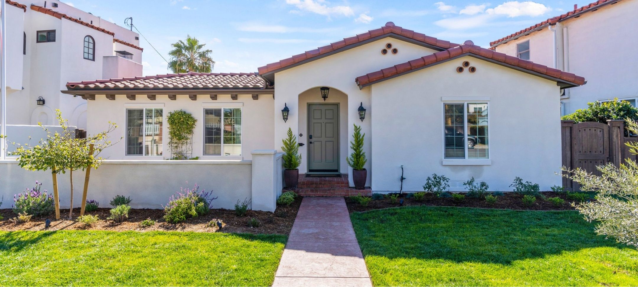Spanish-style custom home with terracotta tile roof, arched entry, and landscaped front walkway