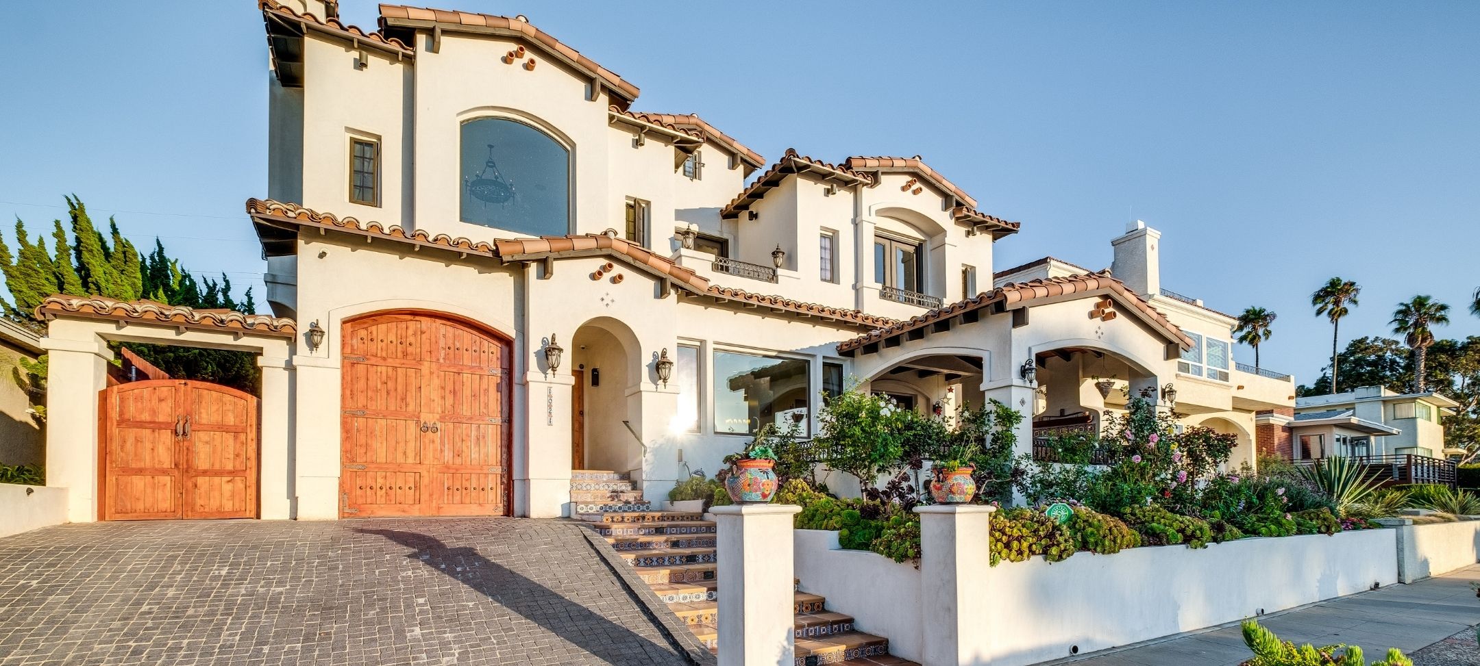 Spanish-style custom home with clay tile roof, carved wood garage doors, and tiled entry steps
