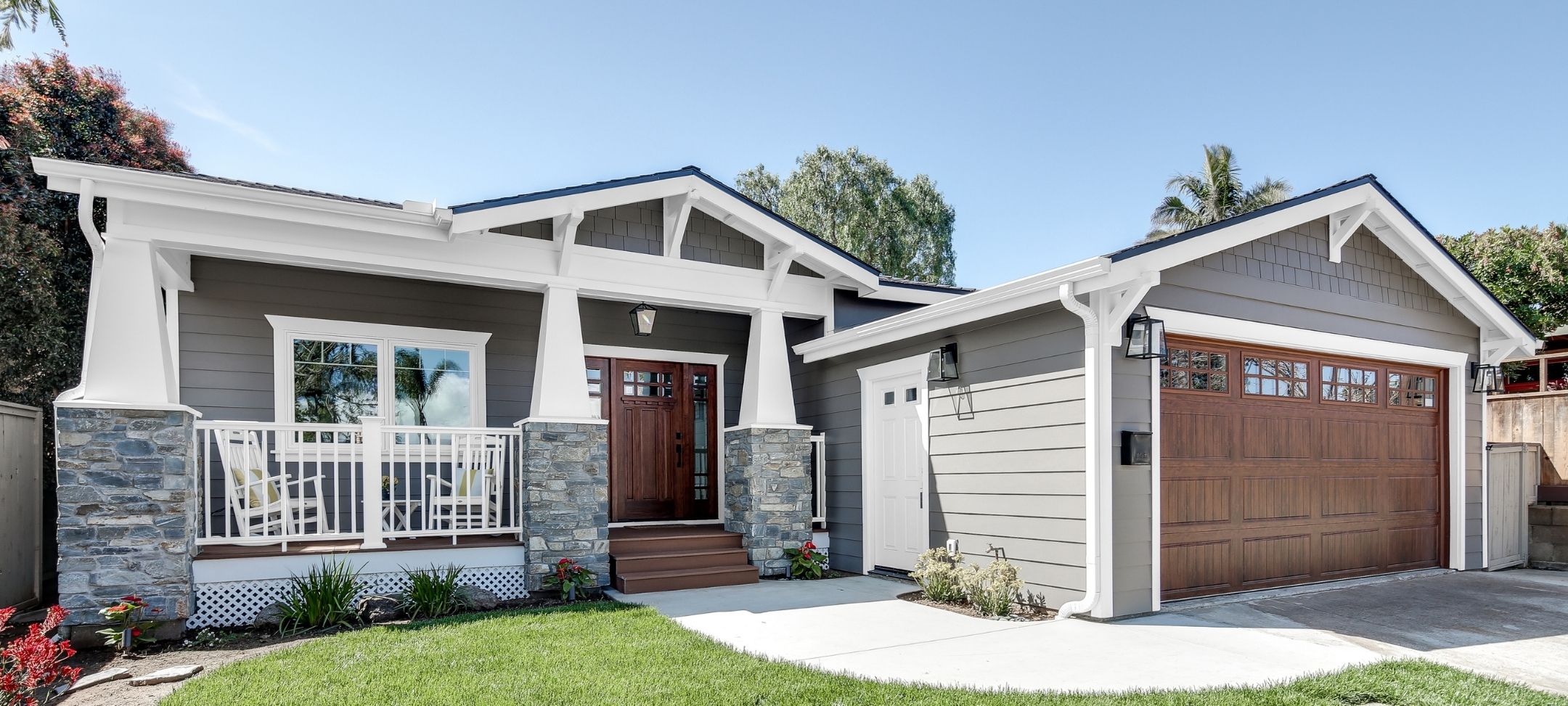 Craftsman custom home with gray siding, stone porch columns, and wood-tone garage doors