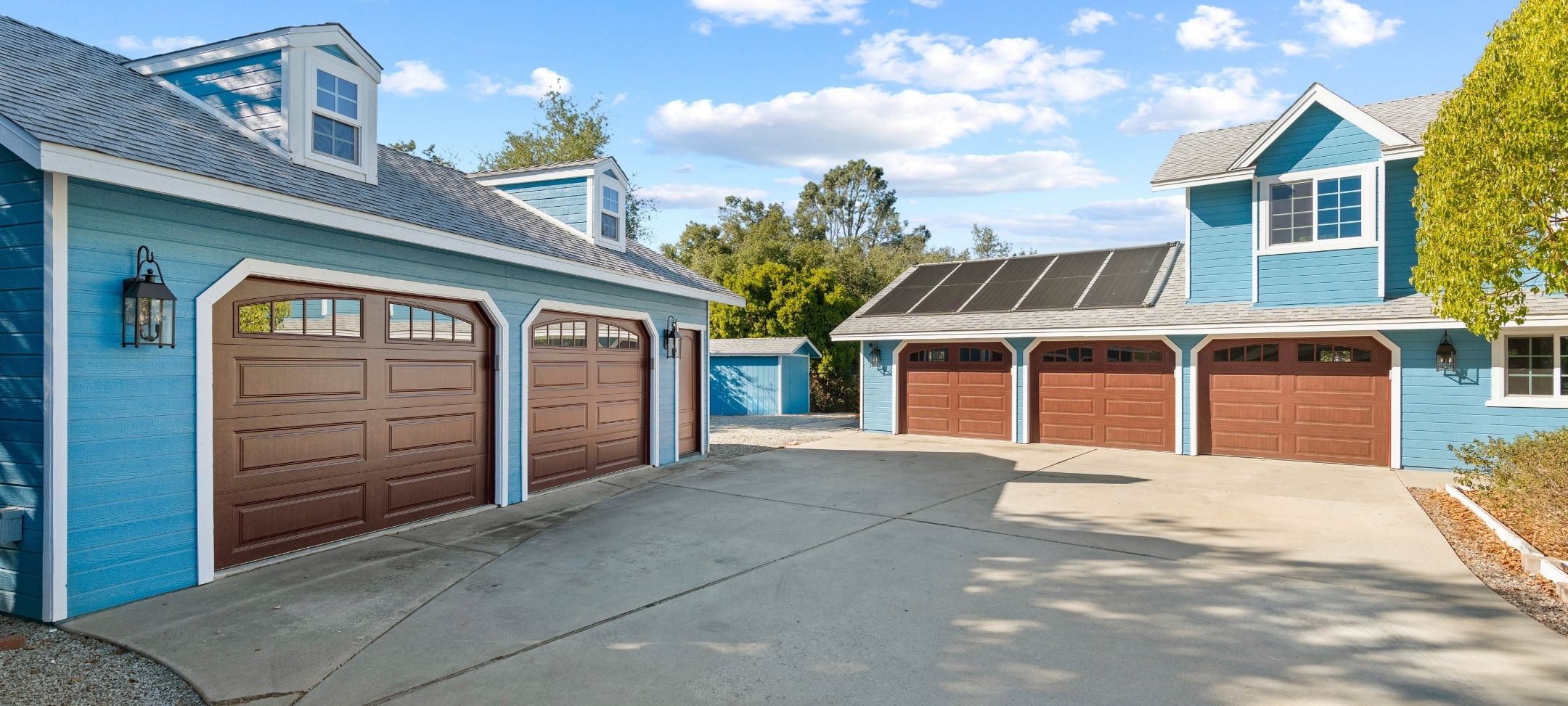 Custom home multi-car garage building with blue siding, wood-tone doors, and rooftop solar panels