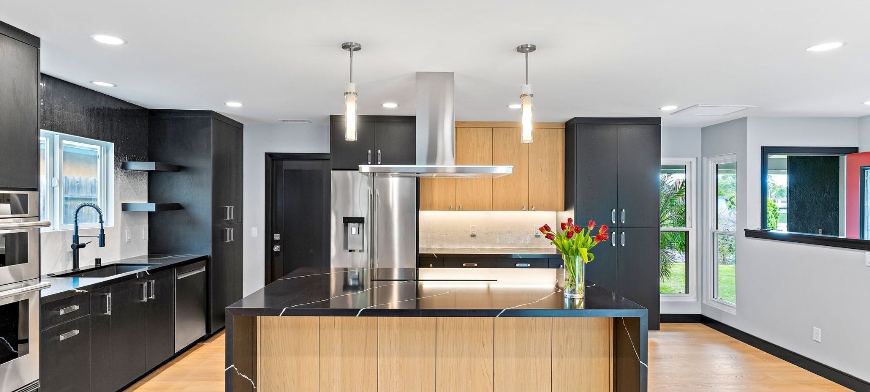 Modern kitchen remodel with black cabinetry, waterfall wood island, and stainless steel appliances