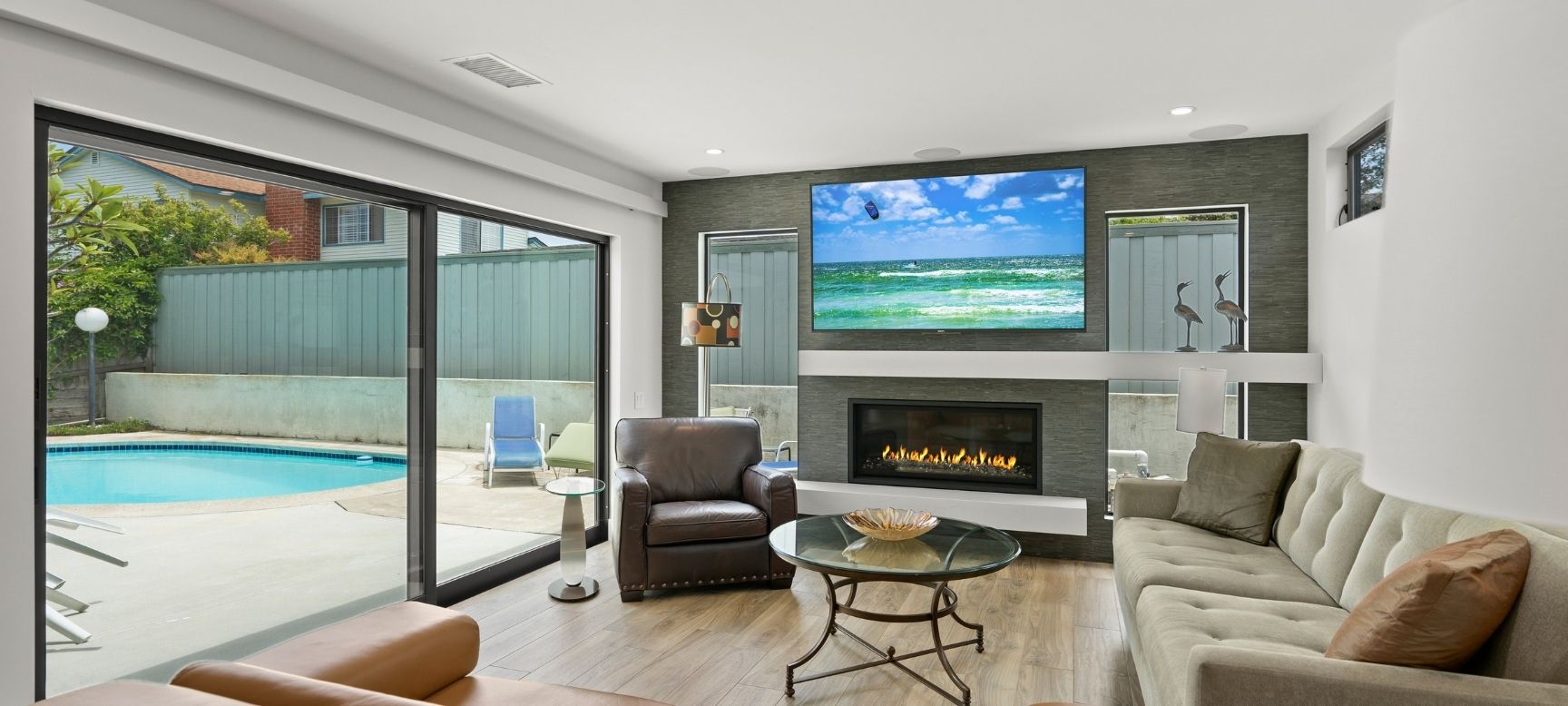 Remodeled living room with gas fireplace, mounted TV, and sliding glass doors opening to the backyard pool