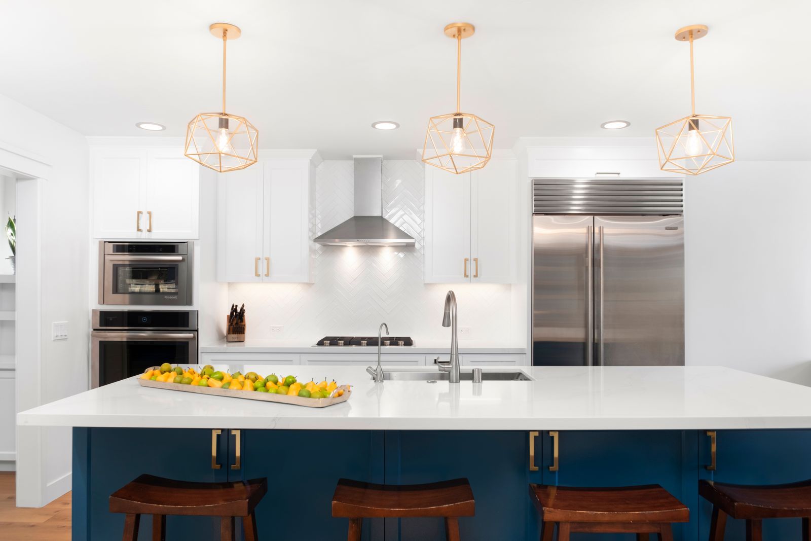 Completed Lars kitchen with a blue island, white cabinetry, brass hardware, and geometric pendant lights