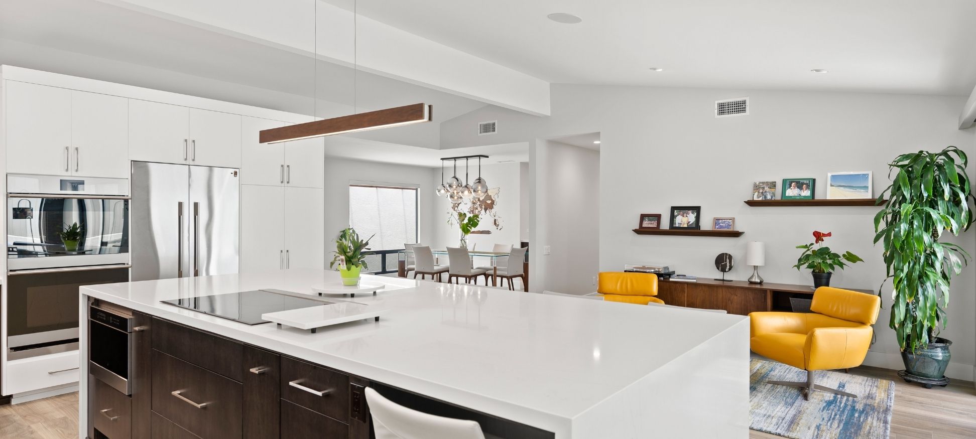 Open-concept kitchen and living room remodel with dark wood island, wood pendant light, and yellow leather lounge chairs