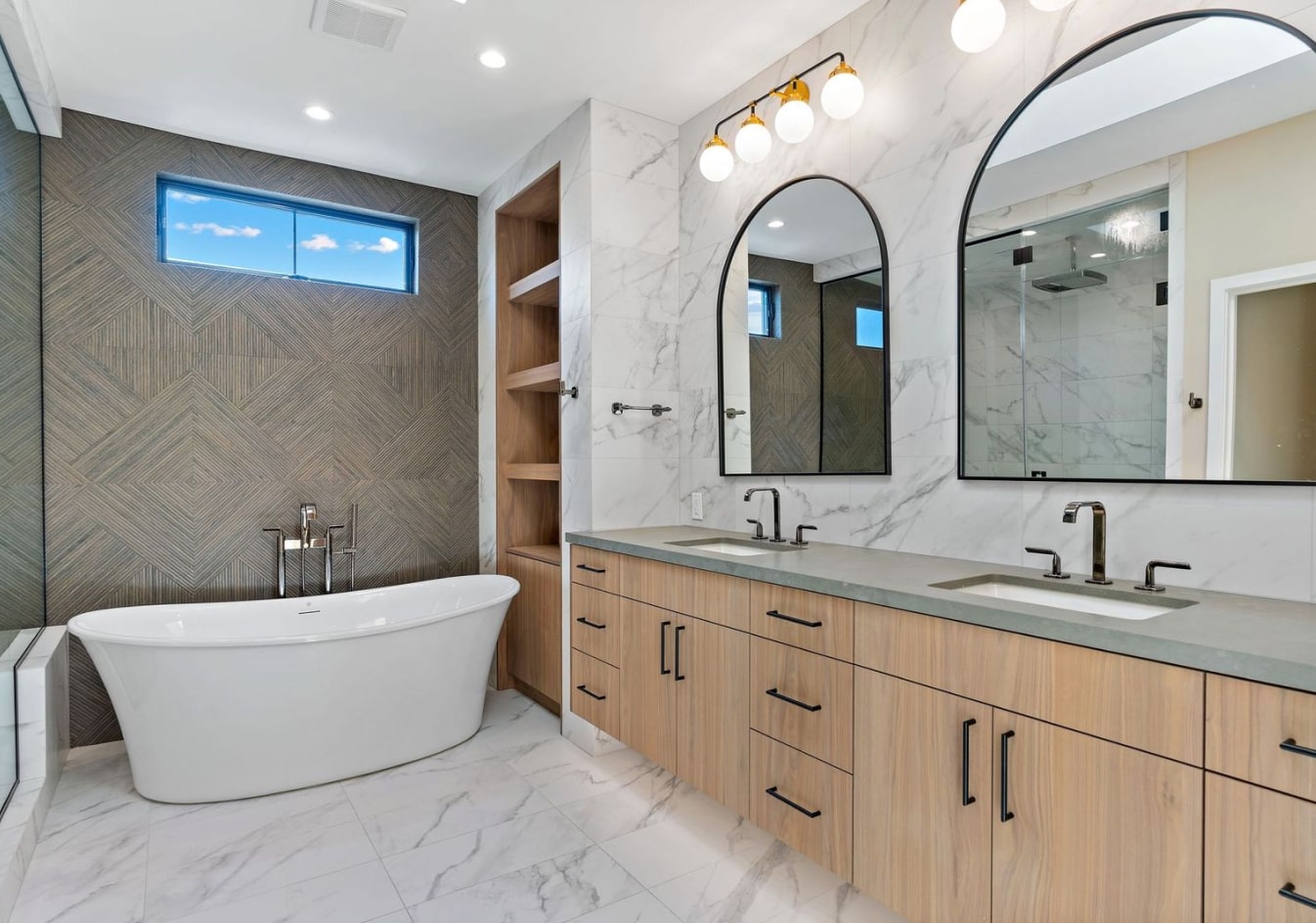 Completed bathroom showing coordinated tile, cabinetry, countertops, lighting, mirrors, and fixtures