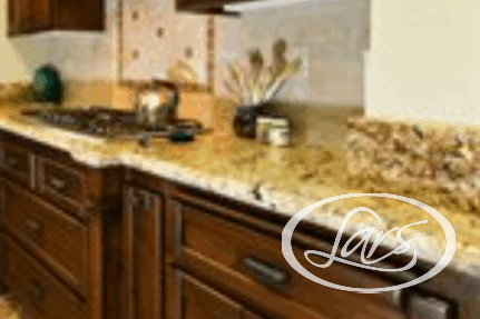 A kitchen with dark wood cabinets and a beige granite countertop. The backsplash features a decorative tile inlay above the stove. There are cooking utensils, a kettle, and a decorative vase placed on the countertop.