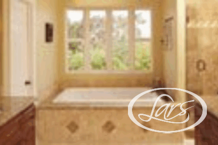 A bathroom with a large tub situated under a wide window with scenic outdoor views. The walls and bathtub enclosure feature beige tiles. To the right, there is a walk-in shower with a glass door. The countertops are granite, and the room has warm lighting.