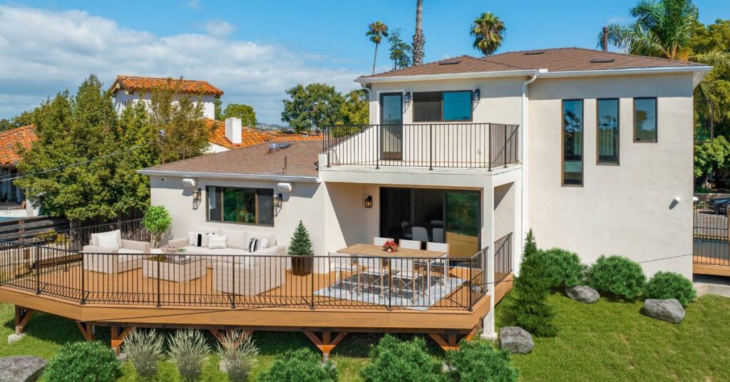 Custom backyard deck design with outdoor seating, dining space, and modern railings attached to a remodeled two-story home, showcasing functional and stylish deck remodeling ideas.