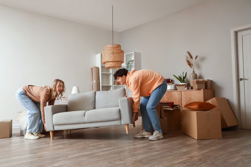 Young couple carrying sofa in room on moving day