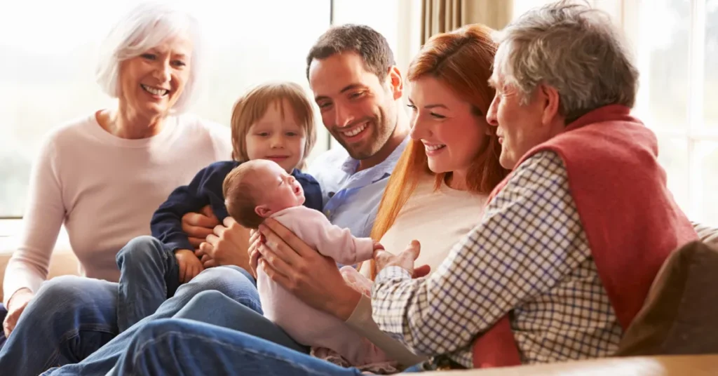 A multi-generational family smiling together while holding a newborn baby.