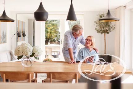 Senior Couple Relaxing With Magazine At Home Looking At Mobile Phone Sitting At Dining Room Table