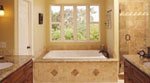 A bathroom with a large tub situated under a wide window with scenic outdoor views. The walls and bathtub enclosure feature beige tiles. To the right, there is a walk-in shower with a glass door. The countertops are granite, and the room has warm lighting.