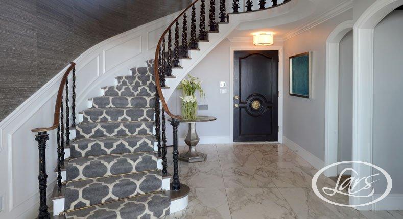 Bottom landing of a luxurious, carpeted staircase with marble flooring.