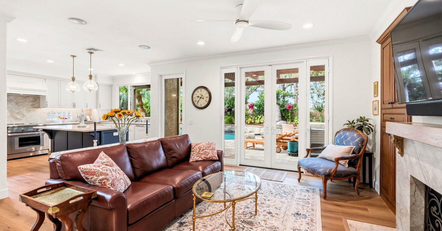 armel Valley whole home remodel — open living room with French doors to backyard pool, kitchen visible in background, marble fireplace surround, and wide-plank hardwood floors, by Lars Remodeling & Design