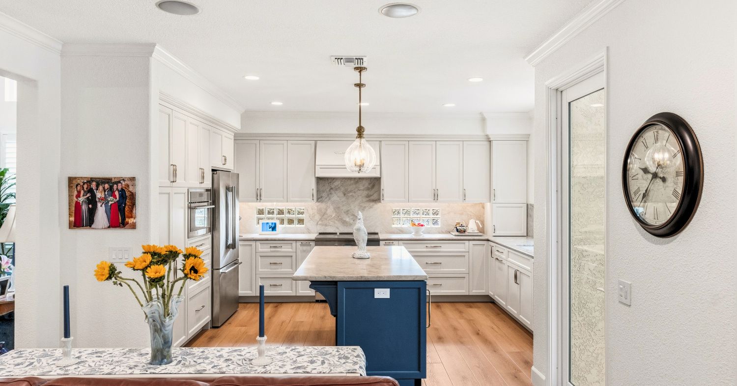 Carmel Valley whole home remodel — full kitchen view with white shaker cabinetry, navy island, stainless appliances, and warm hardwood floors, by Lars Remodeling & Design