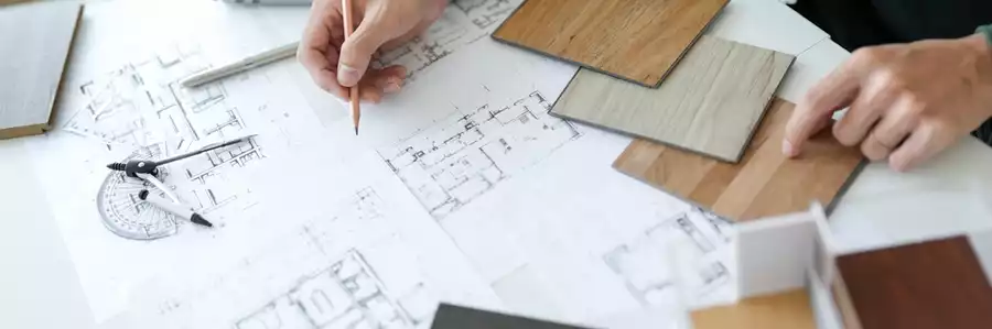 An interior designer looking at floor plans and comparing tile samples.