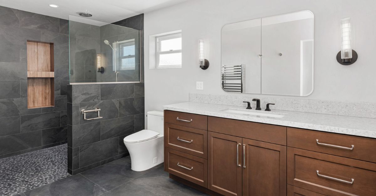 Accessible aging-in-place bathroom with no-threshold walk-in shower, dark tile, and pebble flooring in San Diego remodel.