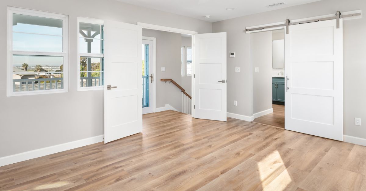 Primary suite entry with barn door, hardwood floors, and balcony access in a Bay Park whole-home remodel and second-story addition by Lars Remodeling & Design.
