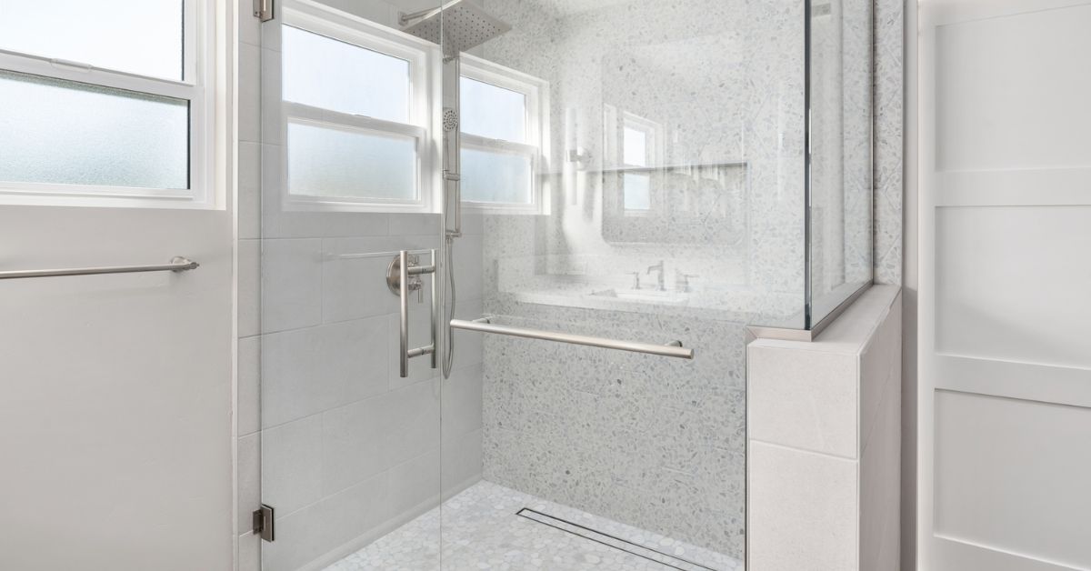 Walk-in shower with terrazzo tile, mosaic floor, rain head, and frameless glass enclosure in the primary bath of a Bay Park whole-home remodel by Lars Remodeling & Design.