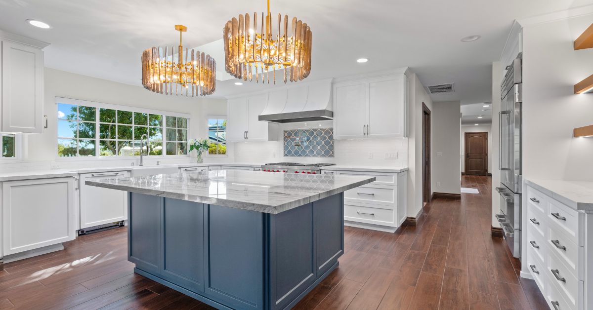 Bright luxury kitchen remodel with white cabinetry, waterfall island, wood flooring, and decorative lighting
