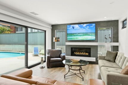 Completed luxury living room remodel with large sliding glass doors, modern fireplace, and open indoor-outdoor design.