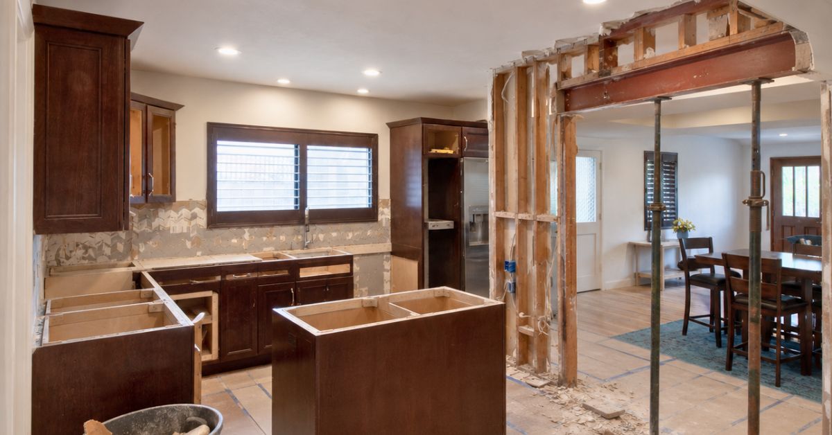 Residential kitchen undergoing structural remodeling with exposed framing, removed walls, and active construction work in progress.