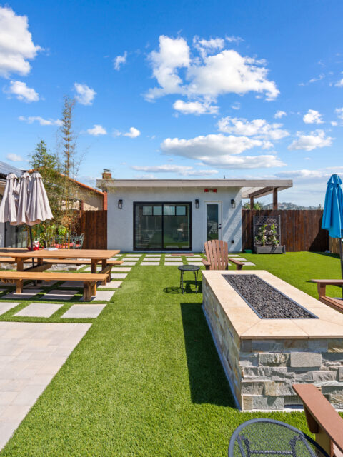 **Alt Text:** Modern backyard accessory structure with artificial turf, a fire pit, outdoor seating, and a landscaped patio.