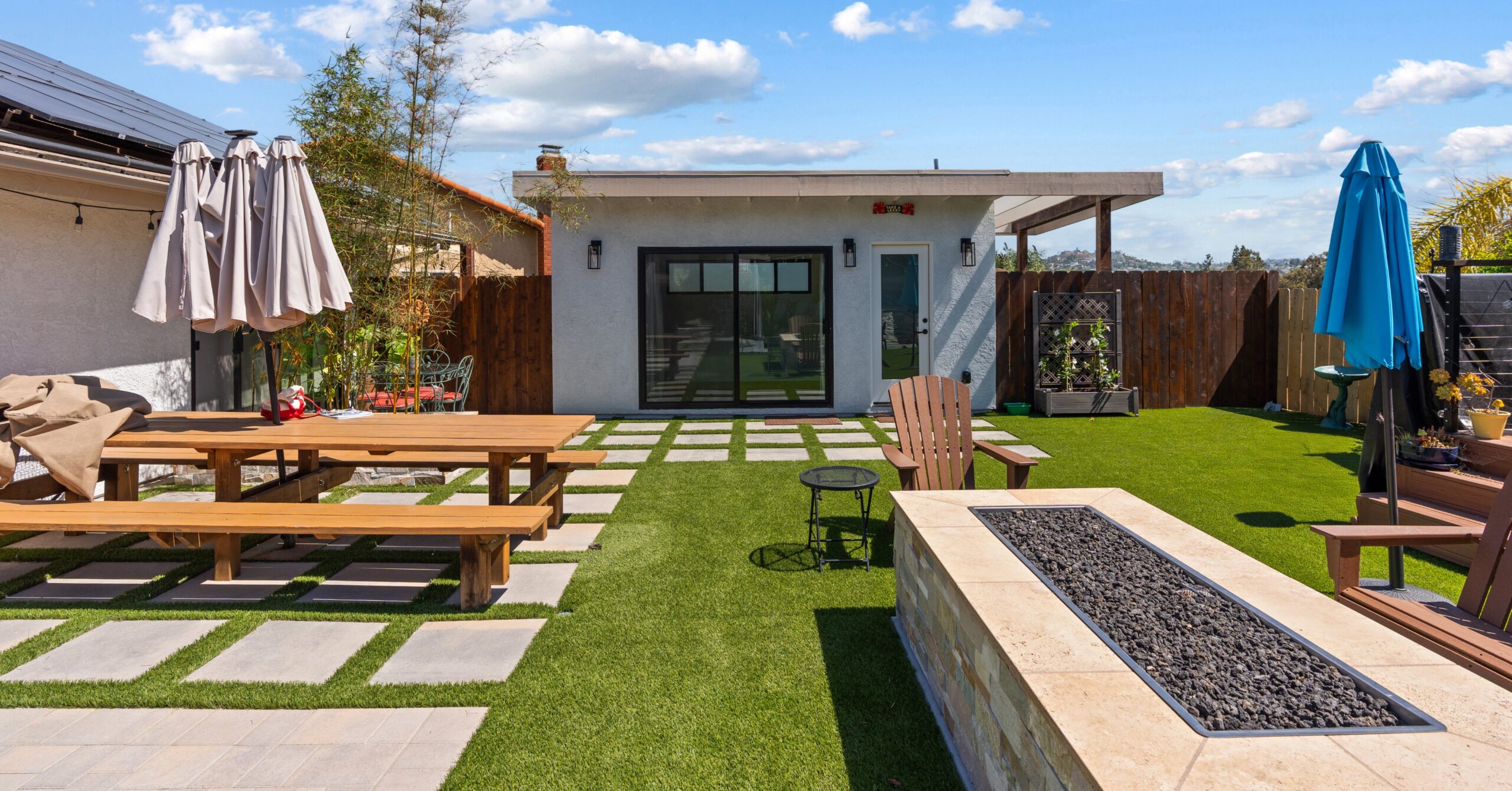 Finished Spring Valley backyard featuring a custom accessory structure, fire pit, artificial turf, large paver patio, and outdoor entertaining space designed to complement the existing pool area.