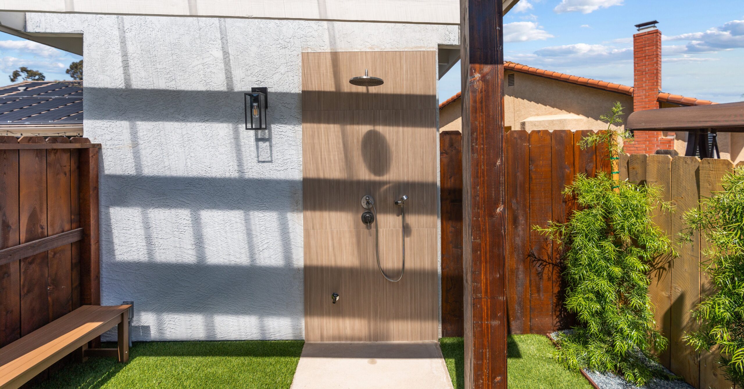 Modern outdoor shower with wood-look tile surround installed beside a custom backyard accessory structure for convenient poolside use.