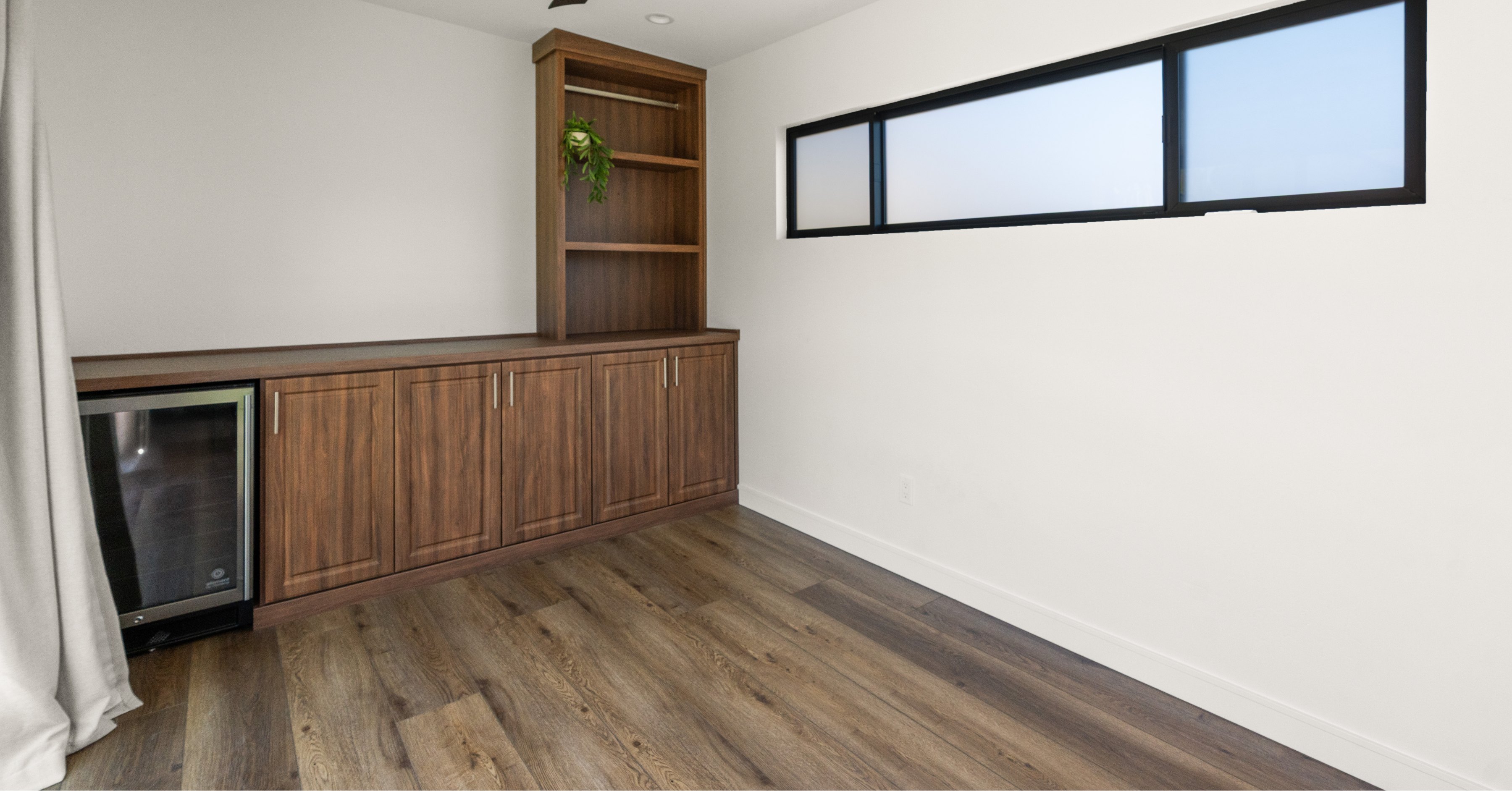 Built-in wood cabinetry with beverage refrigerator and open shelving inside a Spring Valley backyard accessory structure designed for entertaining.