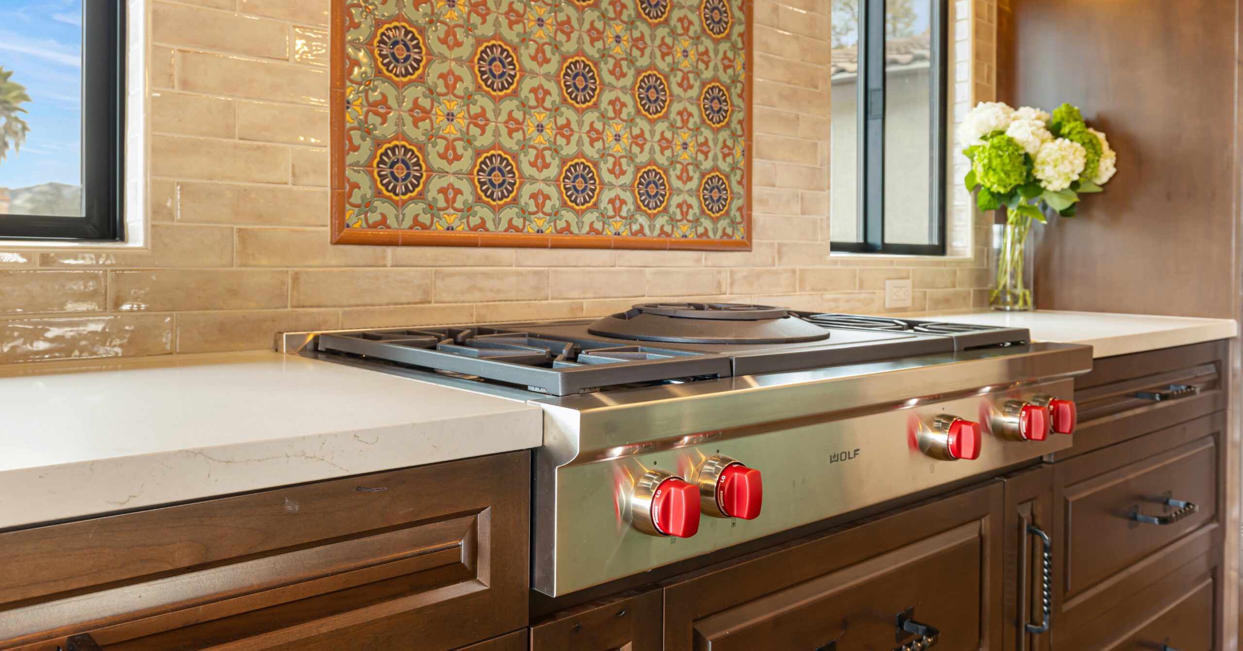 Professional Wolf gas rangetop with red knobs beneath a handcrafted Spanish tile backsplash in a custom Mission-style kitchen remodel.