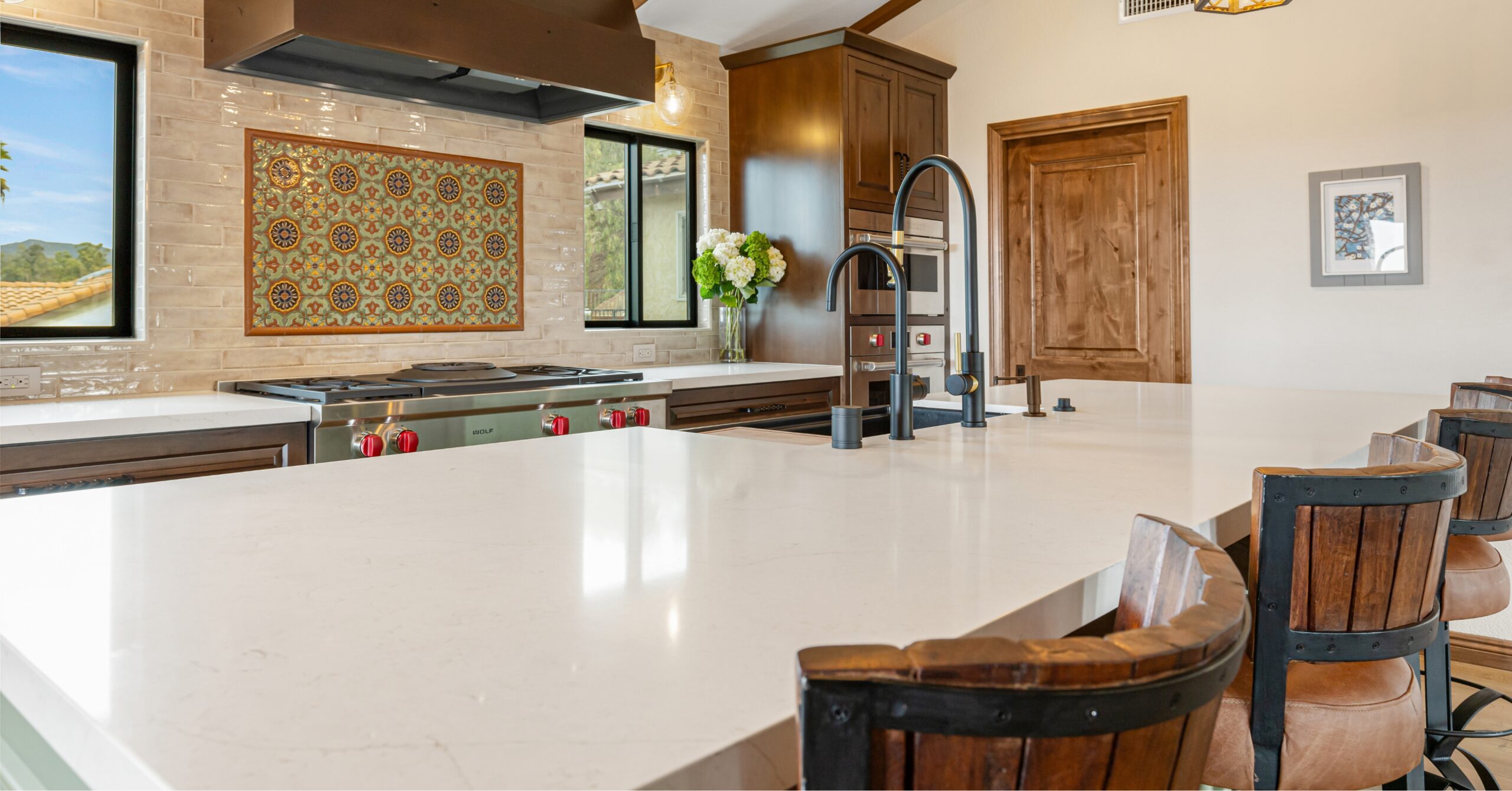 Large quartz kitchen island with seating, farmhouse sink, and custom green cabinetry in an open-concept Mission-Spanish kitchen remodel.
