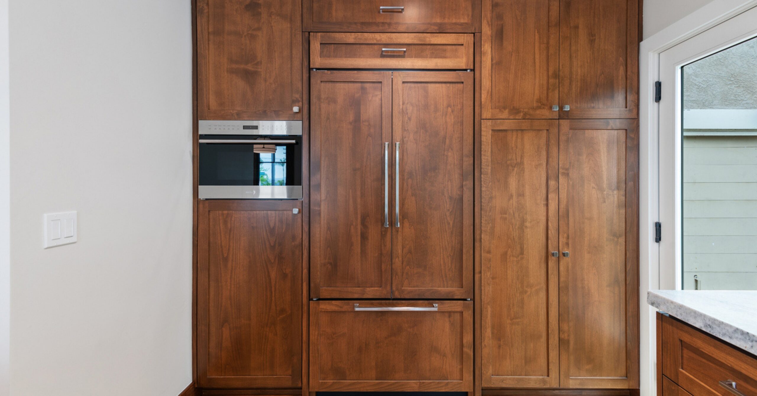 Custom integrated refrigerator and storage wall in a South Park Craftsman kitchen featuring warm wood cabinetry and built-in appliances.