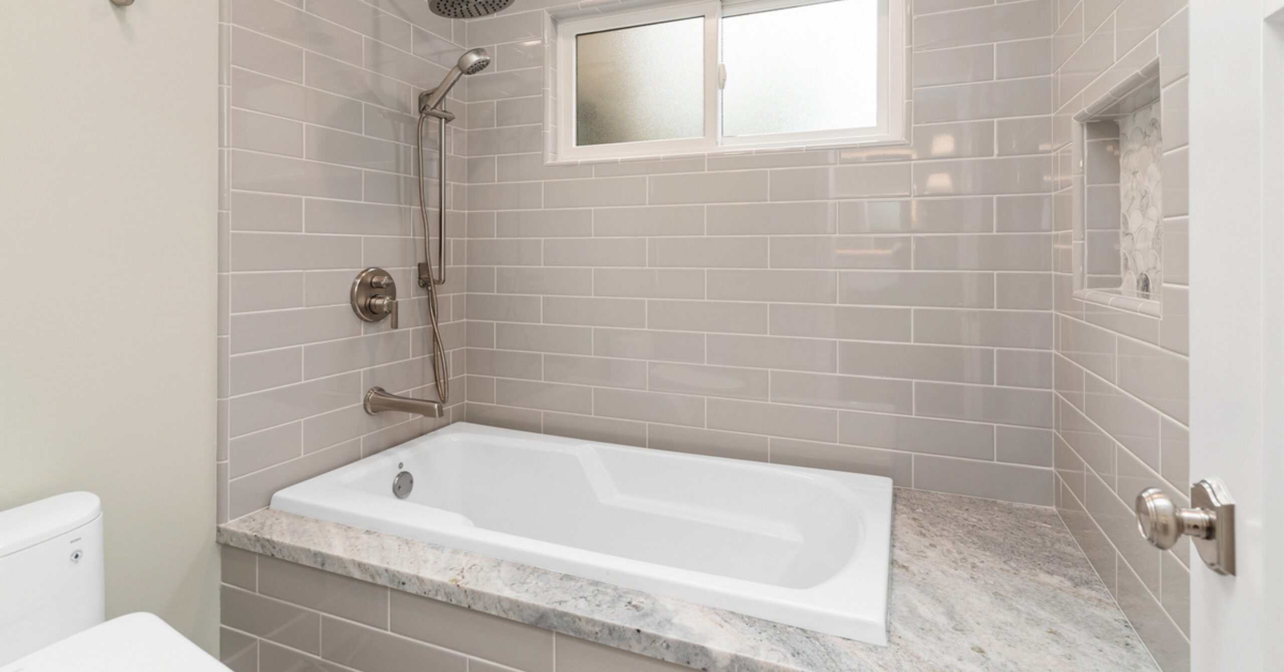 New primary bathroom in a South Park whole-home remodel featuring a soaking tub, subway tile walls, quartz surfaces, and a built-in shower niche.