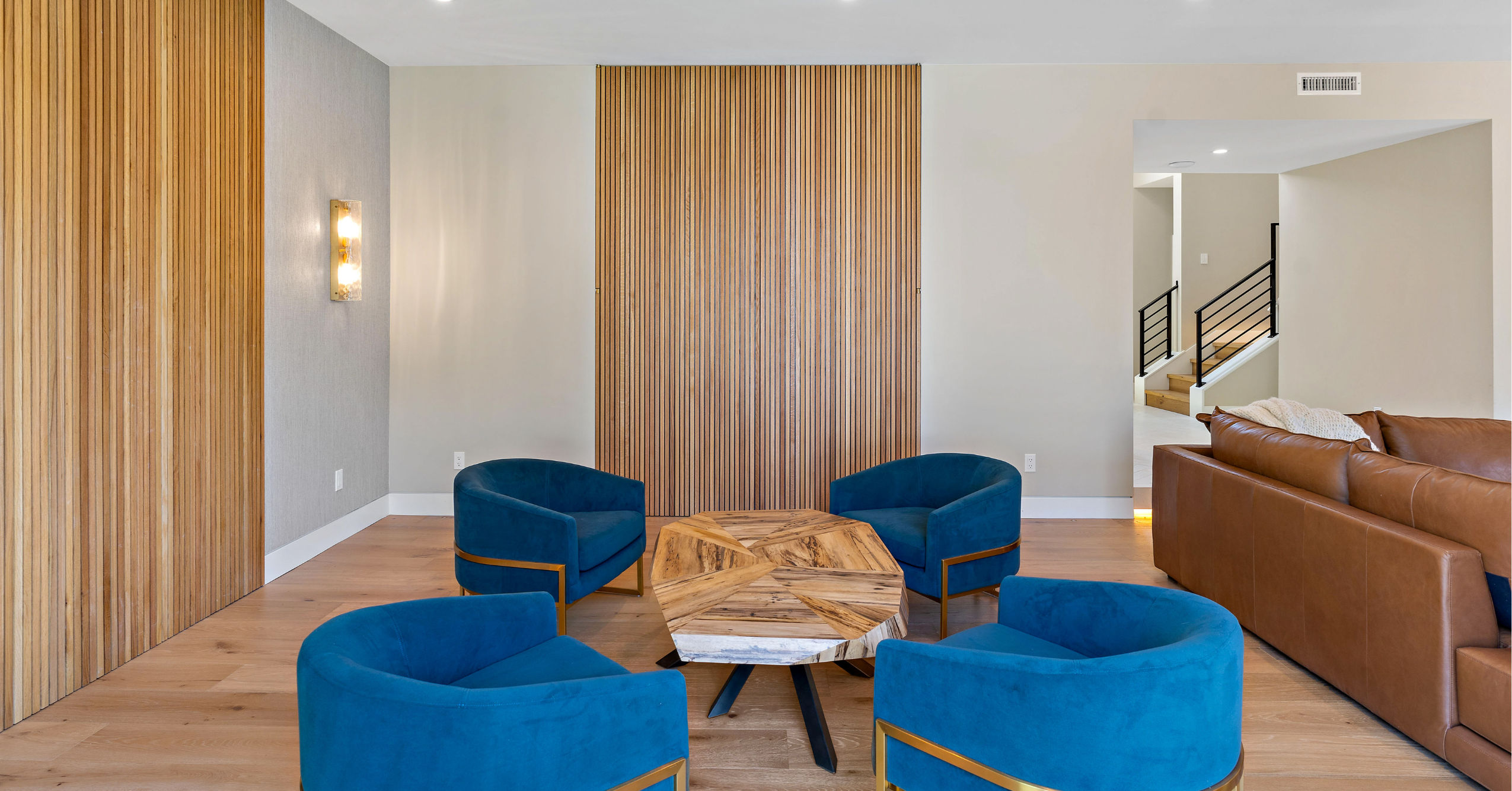 Luxury remodeled living room with custom wood wall panels, blue accent chairs, and upscale contemporary finishes.