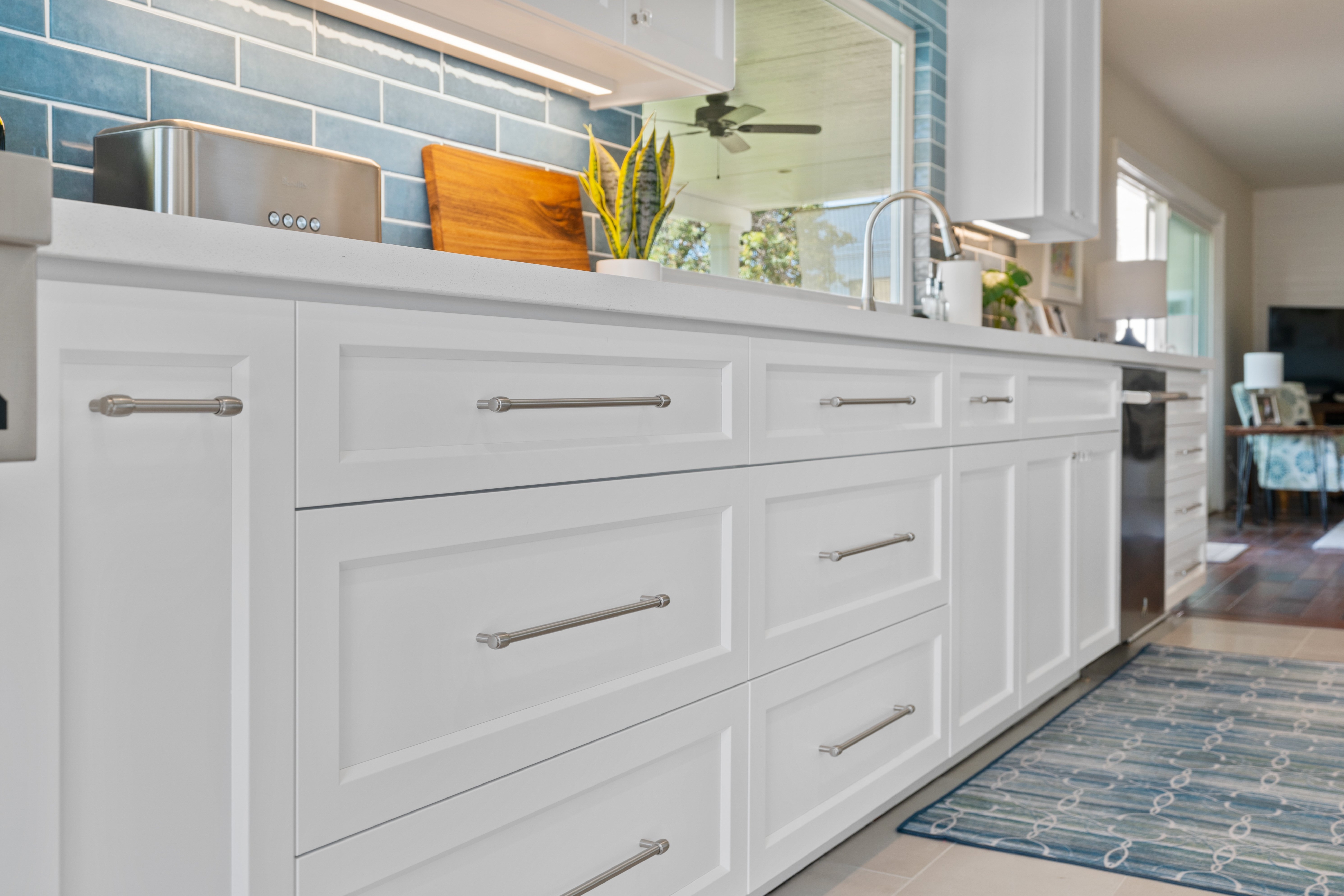 White Shaker kitchen drawers, light countertop, blue subway tile and sink beneath a large window.