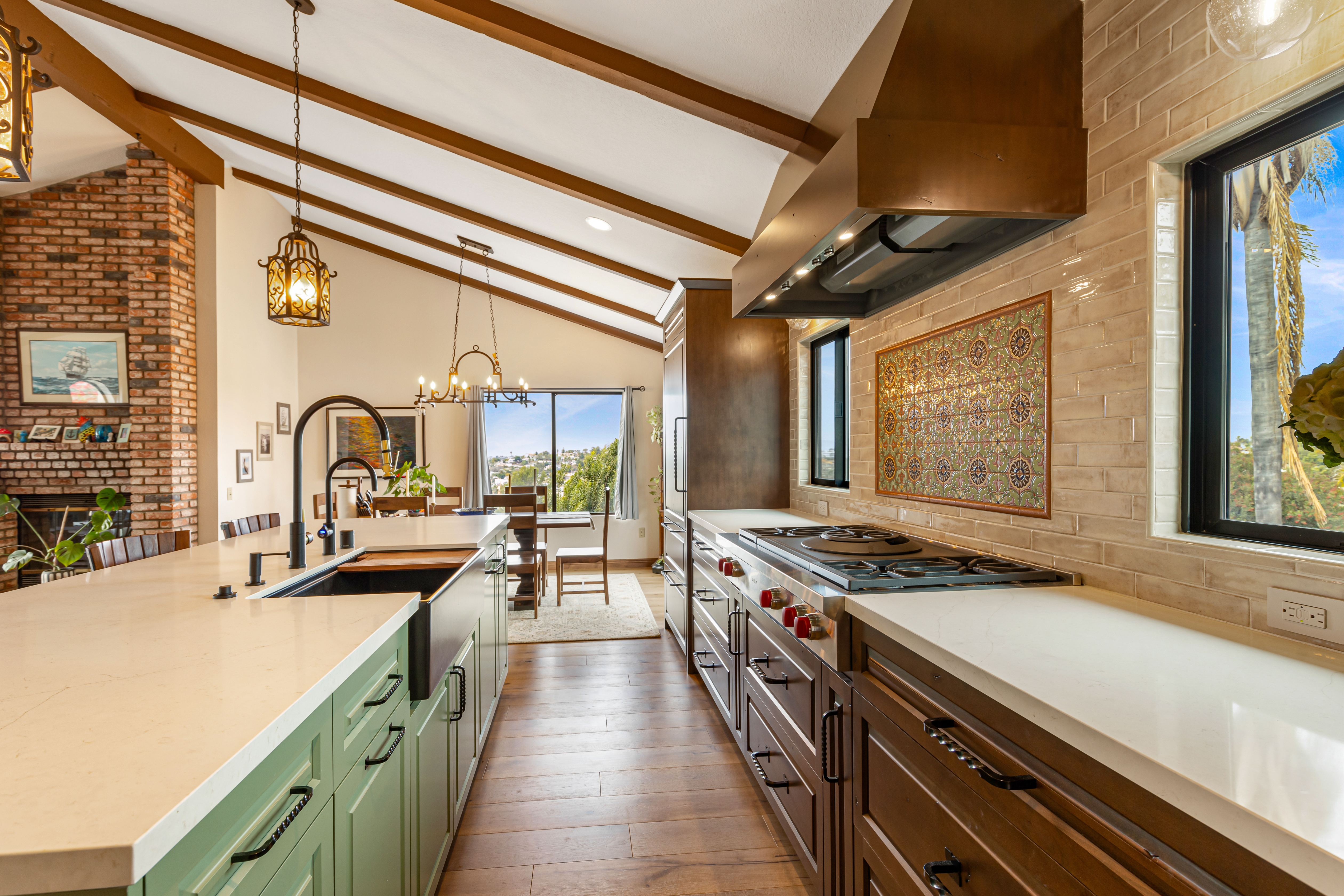 Vaulted Vista kitchen with exposed wood beams, green island, wood cabinetry, white counters and wide range.