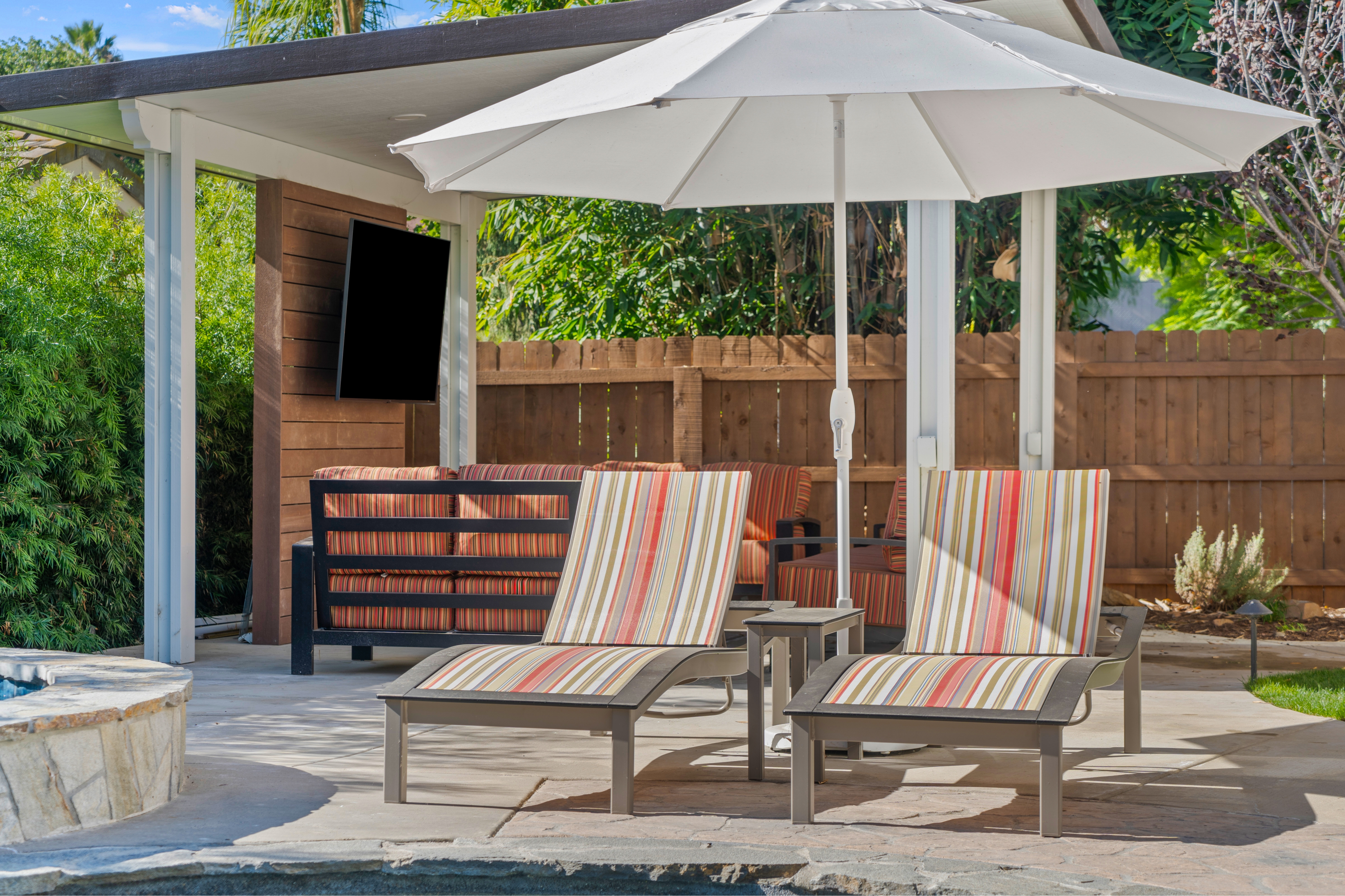 Poolside concrete patio with striped chaise lounges, white umbrella and covered seating area.