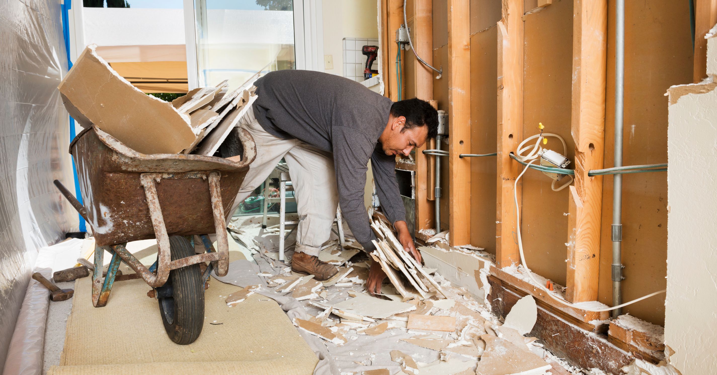 Contractor removing drywall during the demolition phase of a home remodel, exposing framing, plumbing, and electrical systems.