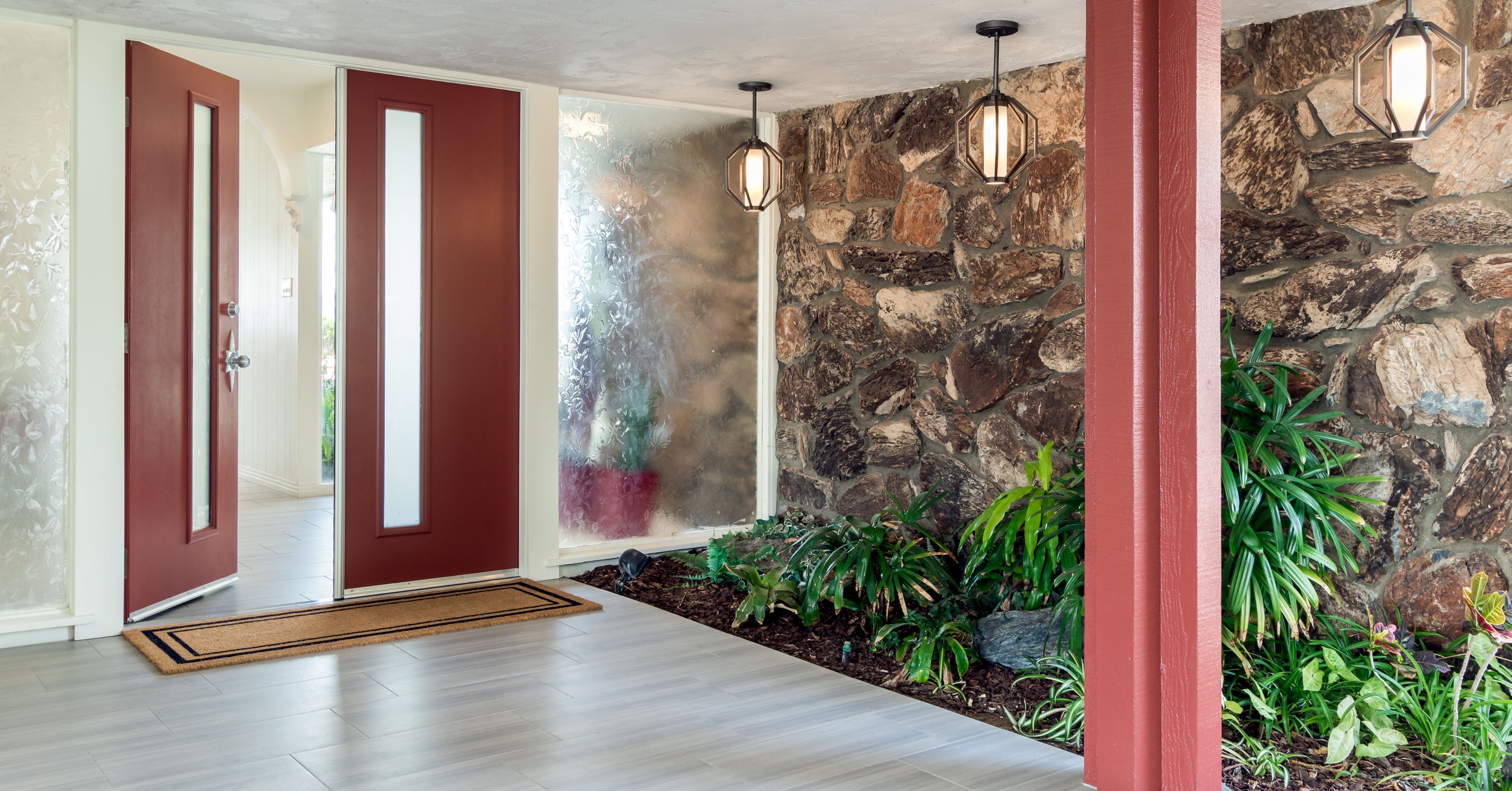 Modern home entryway with pivot front door, stone accent wall, frosted glass panels, and indoor planter following a design-build remodel.