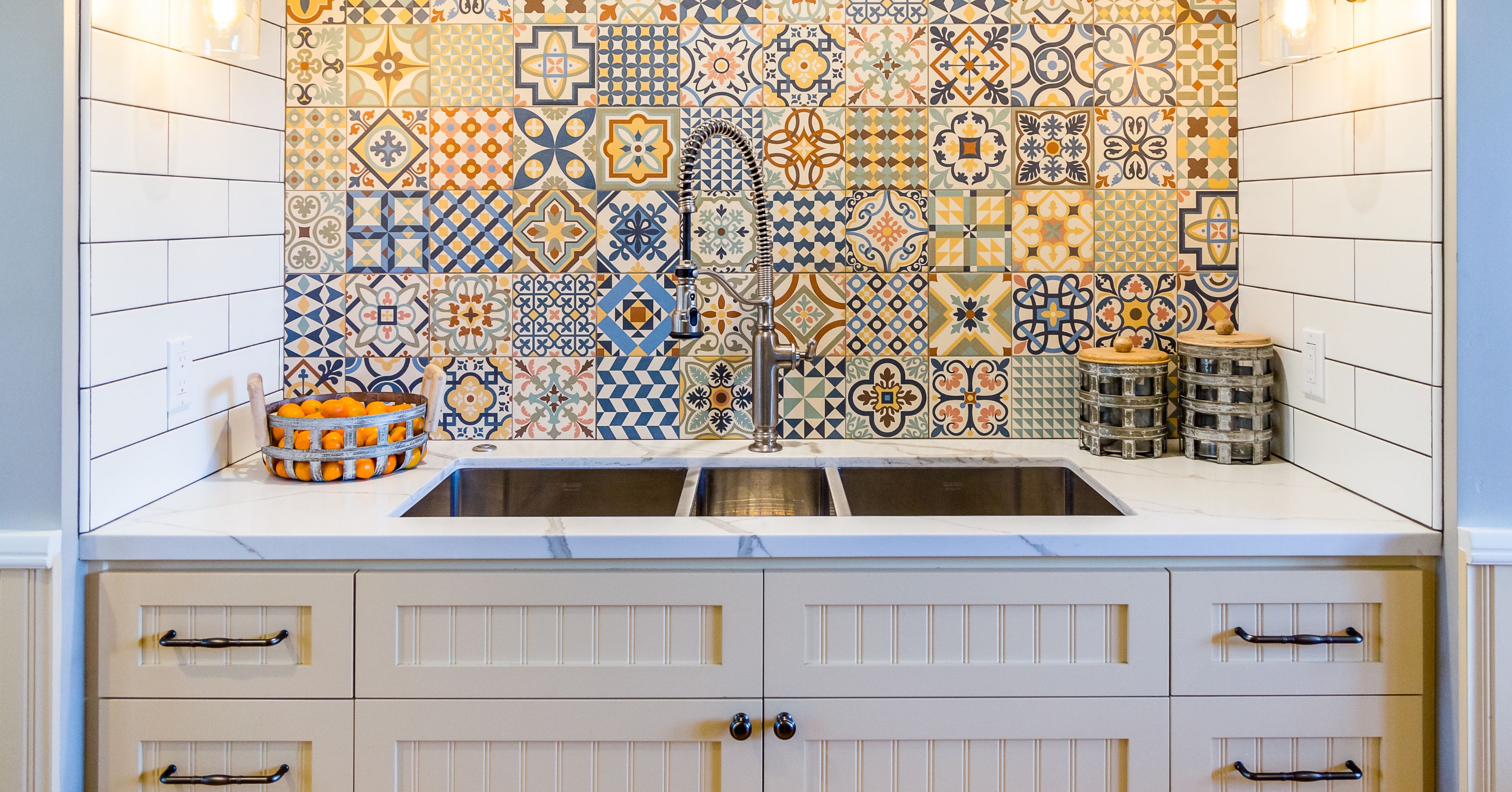 Double-basin workstation sink with quartz countertops, white cabinetry, and a colorful patterned tile backsplash designed for a functional, low-maintenance kitchen.