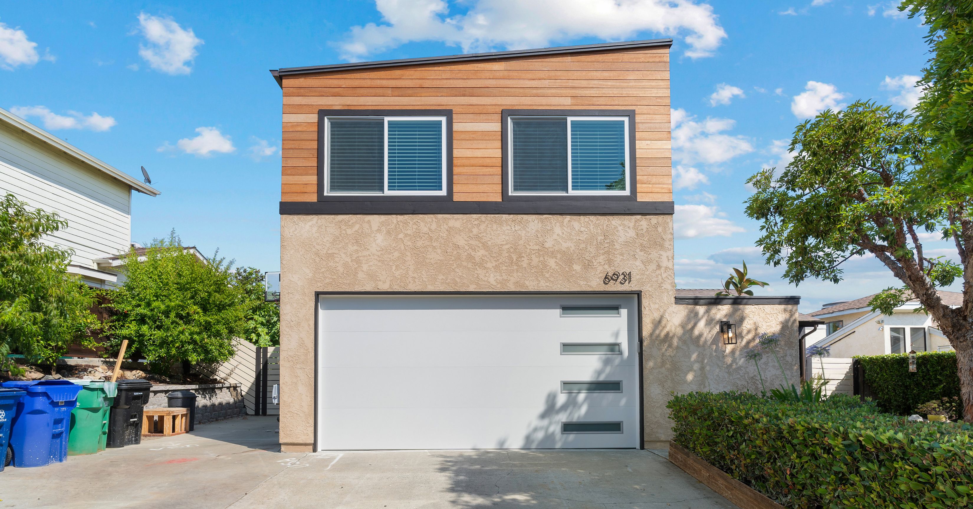 Modern two-story home featuring a contemporary second-story addition with wood siding, large windows, and an attached garage in San Diego.