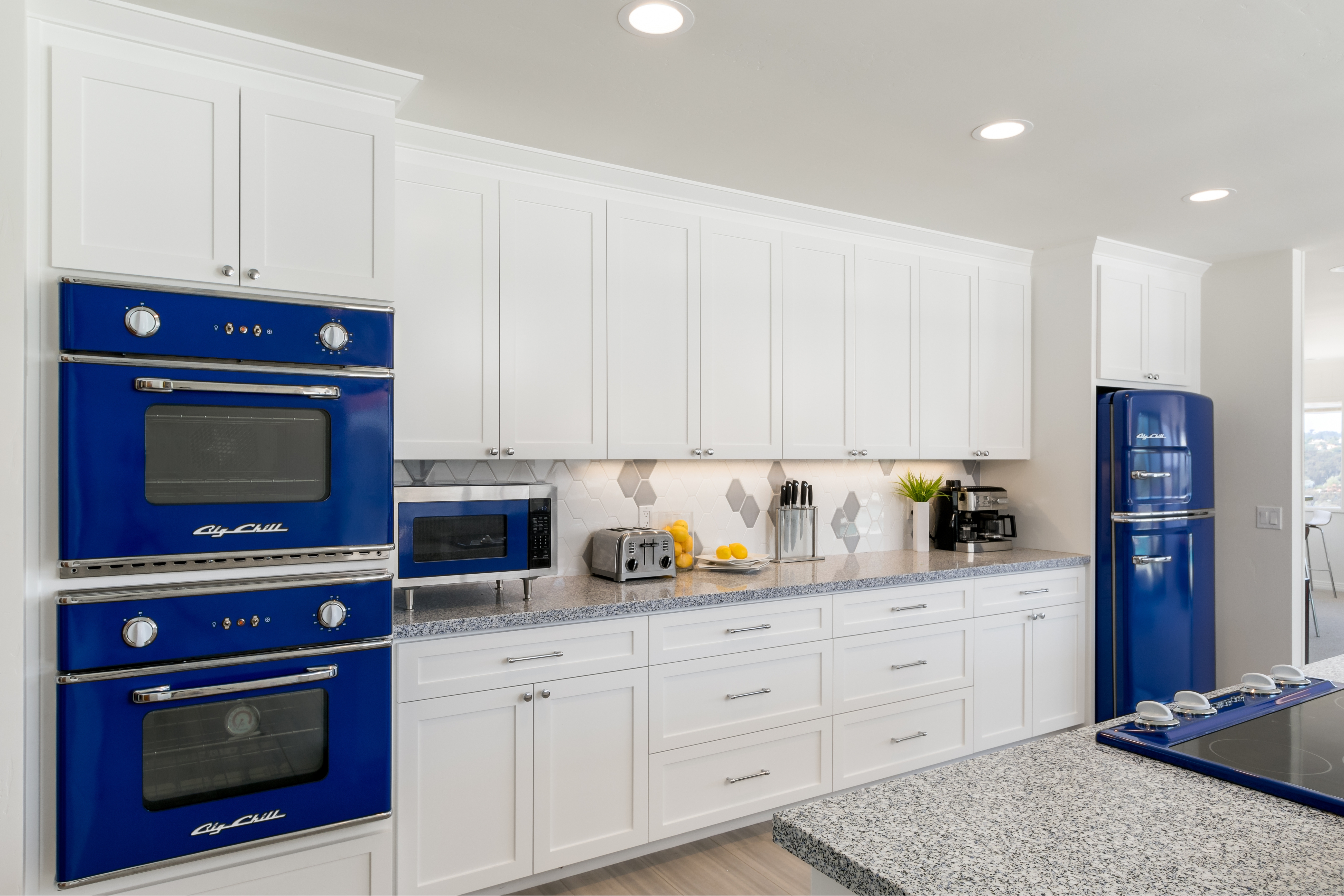 White kitchen with blue retro appliances, shaker cabinetry and gray granite counters.