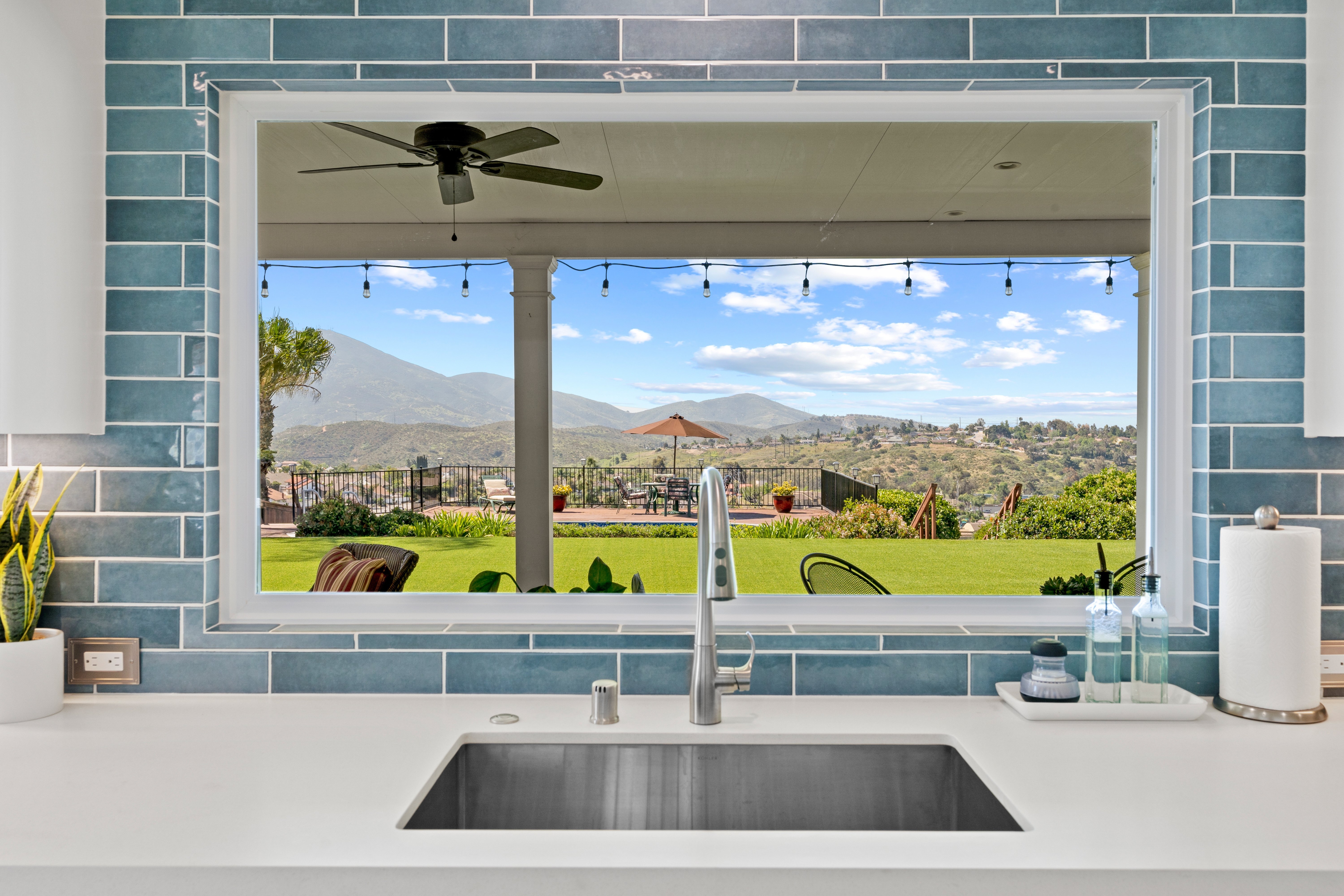 Kitchen sink beneath a large picture window with blue subway tile and a mountain view.